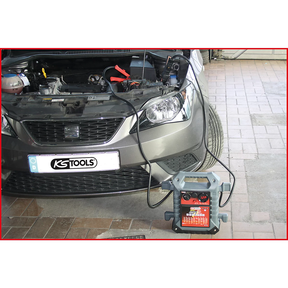 Graues Auto, offene Motorhaube, Starthilfekabel mit Starthilfe-Gerät angeschlossen.